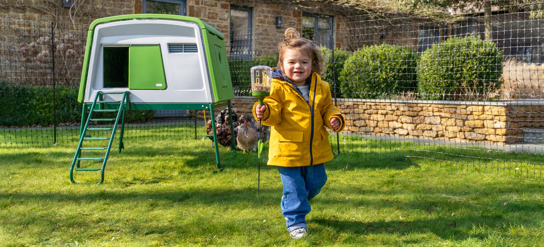 Girl with chicken peck toy next to Eglu Cube large chicken coop and chicken fencing.