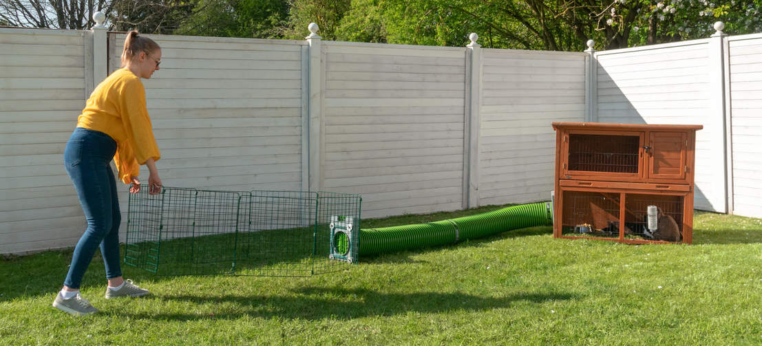 A woman moving a rabbit run which is connected to a wooden rabbit hutch with a zippi tunnel