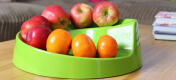 A green rollabowl fruit bowl with lots of fruit on it.