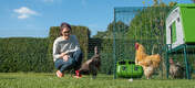 Woman in garden with chickens inside a fenced off area with a large Eglu Cube Chicken Coop