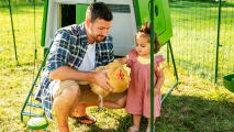 Man with his daughter holding a chicken in a coop run