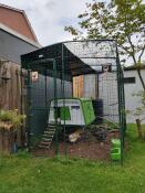 A green chicken coop inside a walk-in run