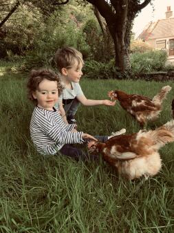 two young children, a boy and a girl feeding chickens in a garden