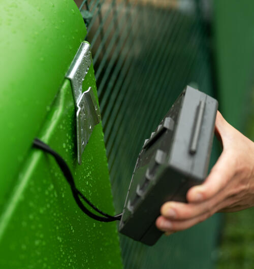 A hand attaching the control panel of the Autodoor to the side of an Eglu Cube chicken coop.