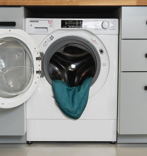 Washing machine with door open and Bolster bed cover in Shaded Spruce print inside.