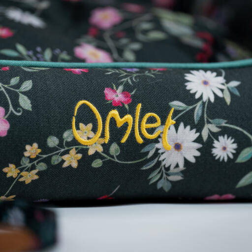 Logo detail on an Omlet Nest Bed in the Midnight Meadow pattern