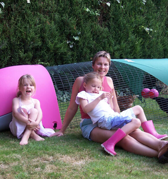 A family sitting next to a pink eglu chicken coop