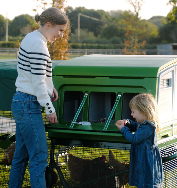 Mother and daughter collecting eggs from green Eglu Pro chicken coop nest box.