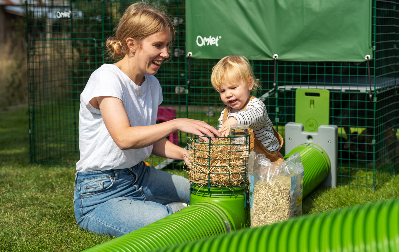 kid adding hay to a large hay rack attached to a guinea pig tunnel burrow