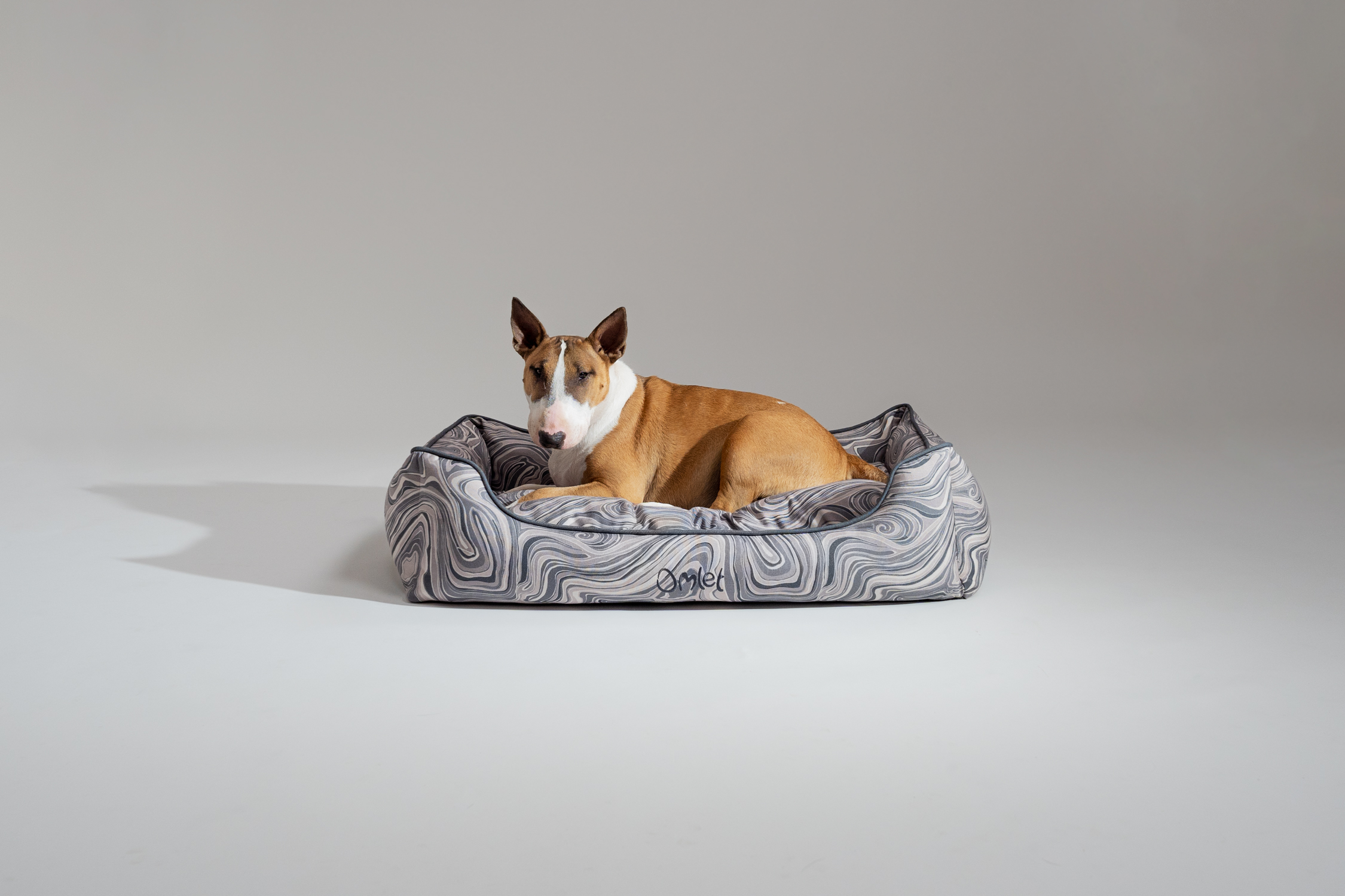 English bull terrier relaxing on their Omlet Nest Dog Bed in Contour Grey