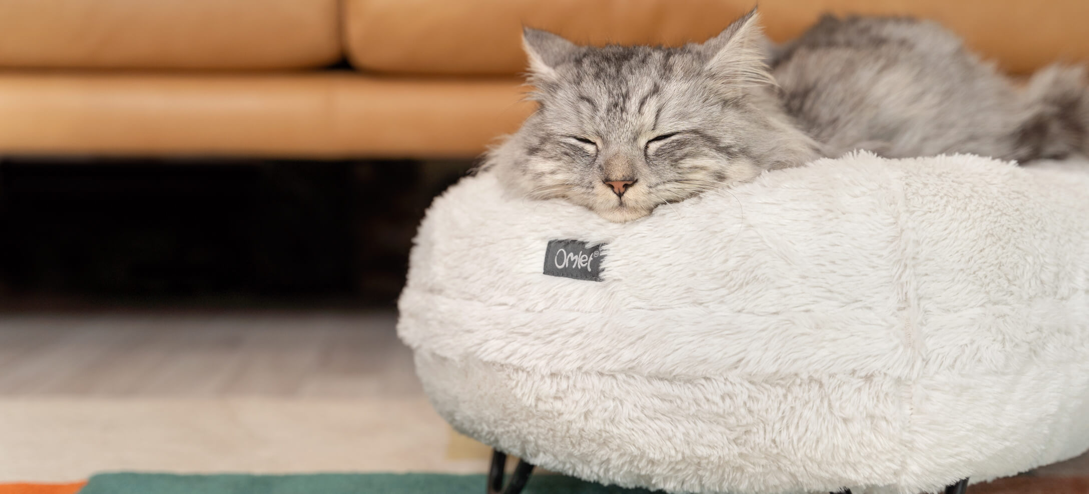 A grey cat sleeping on a white Maya Donut cat bed